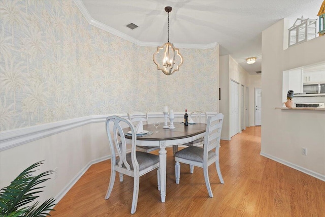 dining space featuring wallpapered walls, a chandelier, light wood finished floors, a wainscoted wall, and crown molding