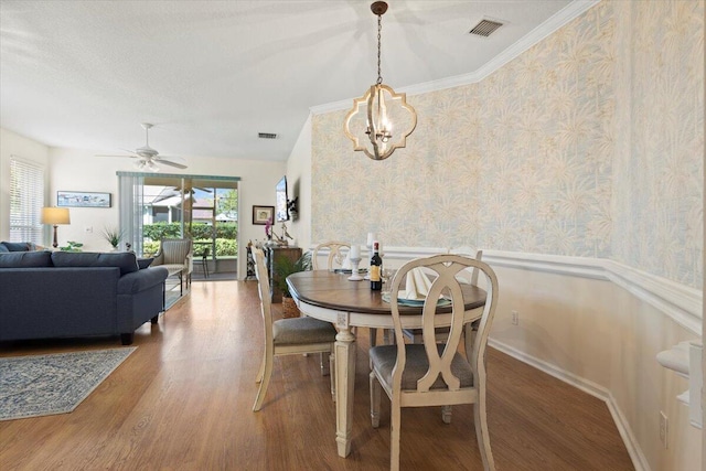 dining room featuring wallpapered walls, wood finished floors, a ceiling fan, a wainscoted wall, and a chandelier