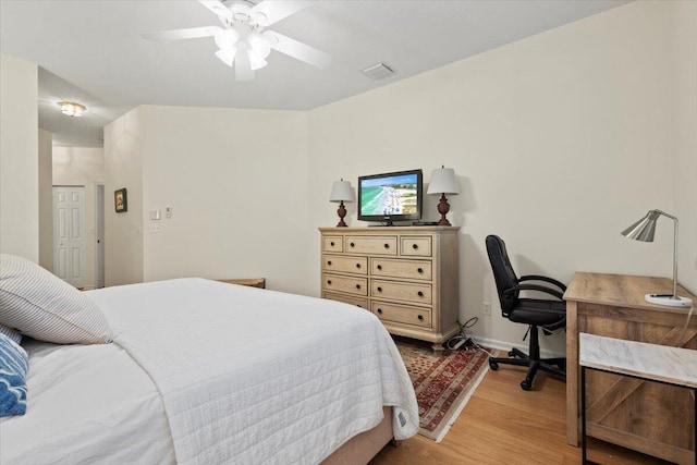 bedroom featuring light wood finished floors, an office area, a ceiling fan, and baseboards
