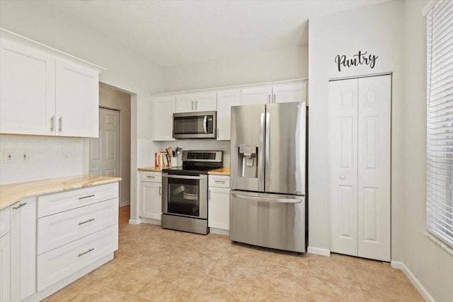 kitchen featuring stainless steel appliances, decorative backsplash, white cabinetry, and baseboards