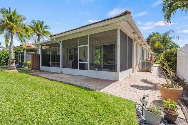 rear view of house featuring a sunroom, a yard, central AC, a patio, and a tiled roof