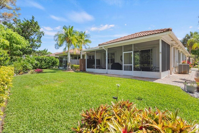 back of house featuring a sunroom, a tiled roof, a lawn, and central AC