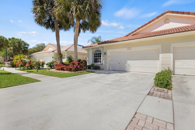 mediterranean / spanish house with concrete driveway, a tiled roof, an attached garage, and stucco siding