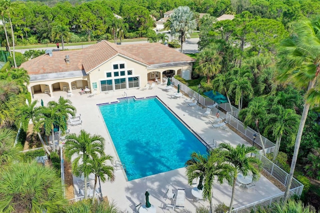 community pool with a patio area, fence, and view of wooded area