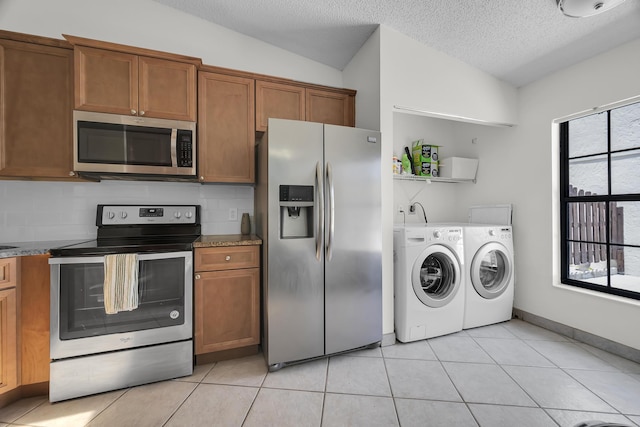 kitchen with stainless steel appliances, separate washer and dryer, brown cabinetry, a textured ceiling, and light tile patterned flooring