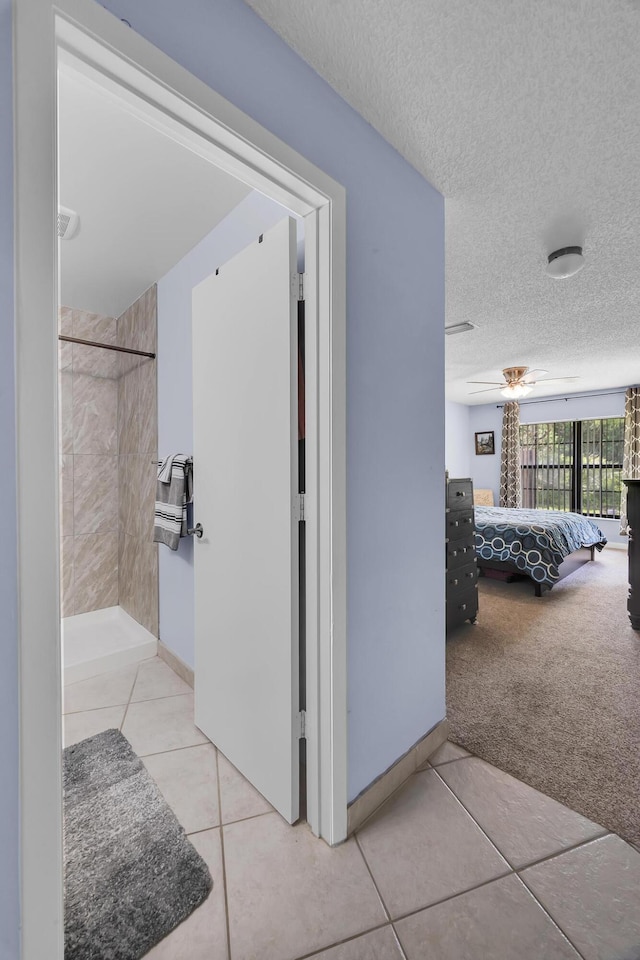 hallway with tile patterned flooring, a textured ceiling, carpet floors, and baseboards