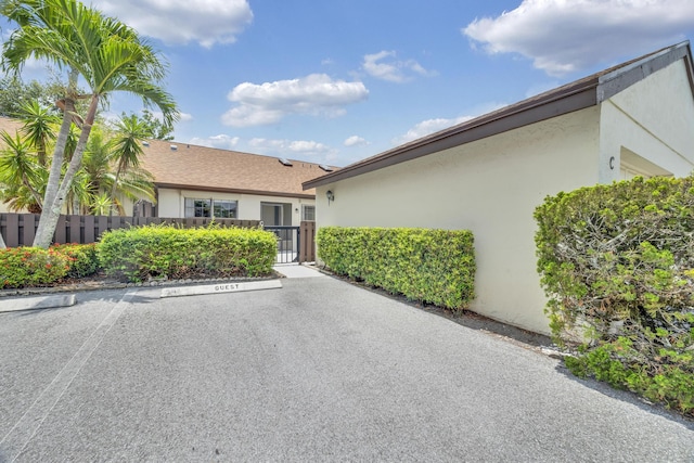 view of front facade with uncovered parking, a gate, stucco siding, and fence