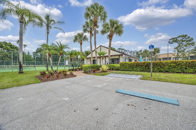 view of community with fence, a tennis court, and uncovered parking