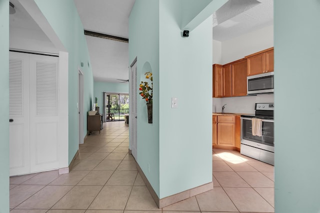 hall featuring light tile patterned flooring, a sink, baseboards, and a towering ceiling
