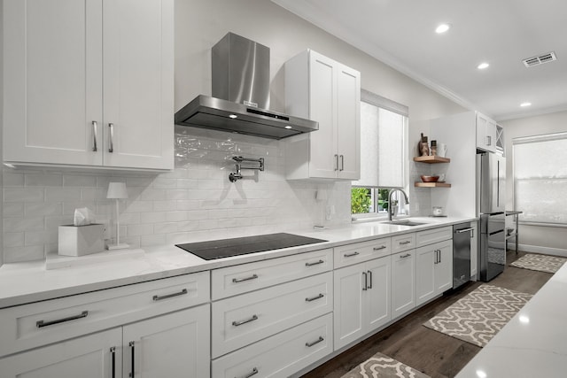 kitchen featuring wall chimney exhaust hood, black electric stovetop, a sink, ornamental molding, and white cabinets