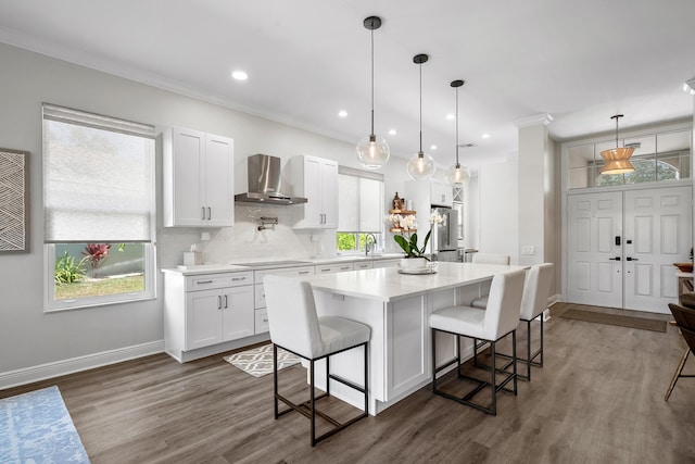 kitchen featuring wall chimney exhaust hood, white cabinets, a kitchen bar, light countertops, and dark wood finished floors