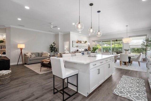 kitchen with white cabinetry, ornamental molding, a kitchen island, open floor plan, and light countertops