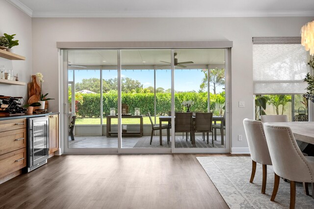 doorway with wine cooler, wood finished floors, crown molding, healthy amount of natural light, and a dry bar