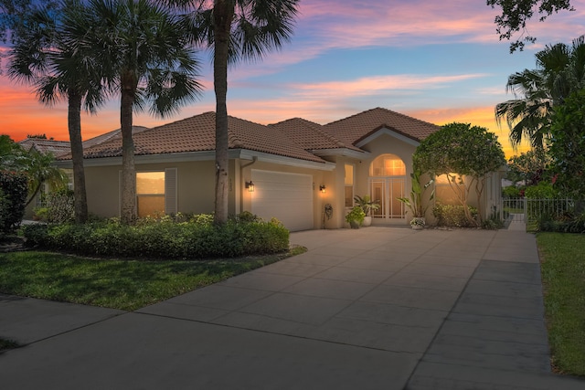 mediterranean / spanish-style home with a tile roof, stucco siding, a garage, fence, and concrete driveway