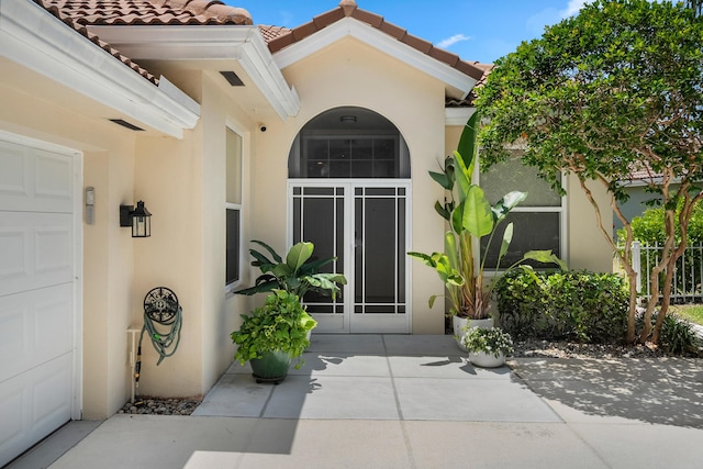 doorway to property featuring stucco siding, a tile roof, and an attached garage