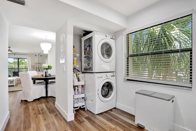 washroom with stacked washing machine and dryer, wood finished floors, baseboards, and a ceiling fan