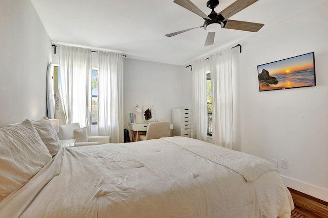 bedroom featuring wood finished floors, baseboards, ceiling fan, and a desk