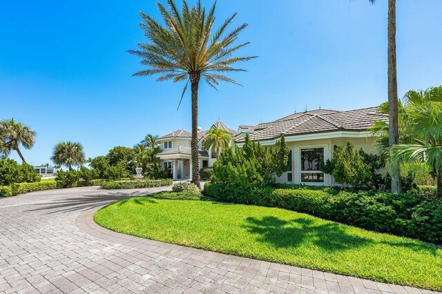 3066 SE Dune Dr, Stuart, FL 34996 - obstructed view of property with curved driveway, a front yard, a tiled roof, and stucco siding