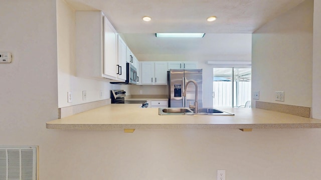 kitchen with appliances with stainless steel finishes, a sink, a peninsula, light countertops, and recessed lighting
