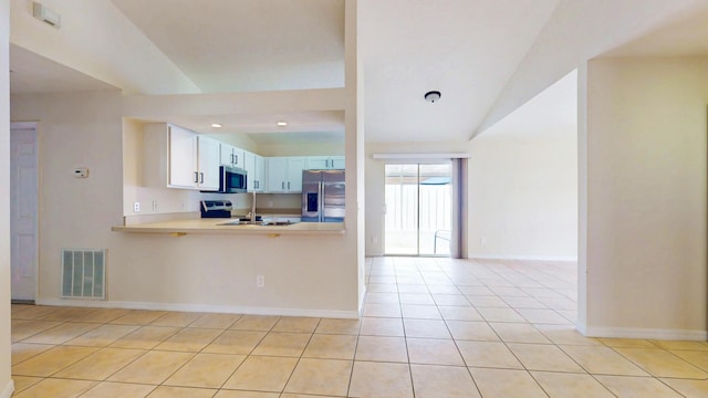 kitchen with appliances with stainless steel finishes, vaulted ceiling, light tile patterned floors, light countertops, and baseboards