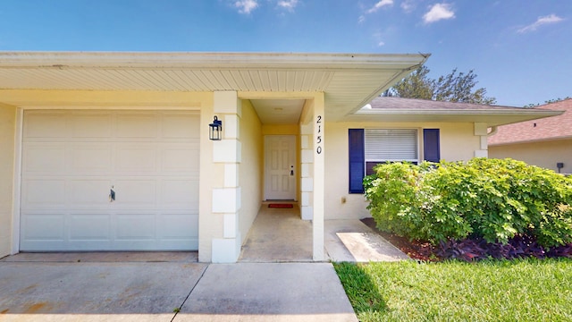 view of exterior entry with stucco siding, a garage, driveway, and a shingled roof