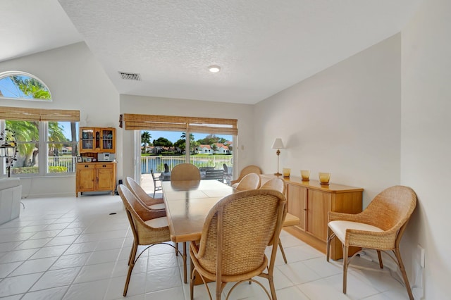 dining area featuring light tile patterned floors, a textured ceiling, a water view, and lofted ceiling