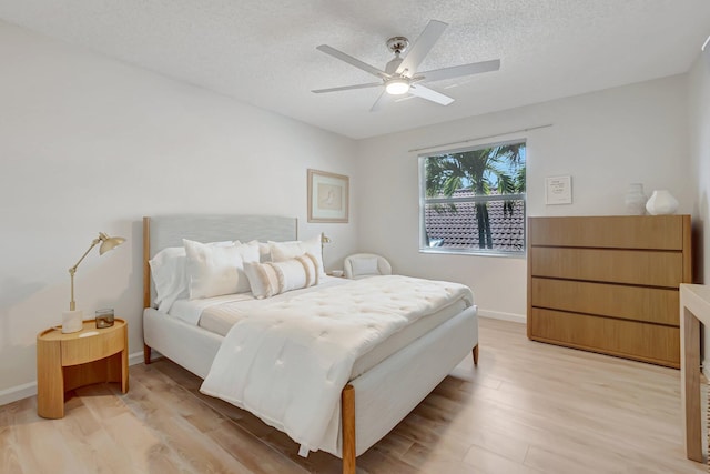 bedroom with light wood-style flooring, a textured ceiling, a ceiling fan, and baseboards
