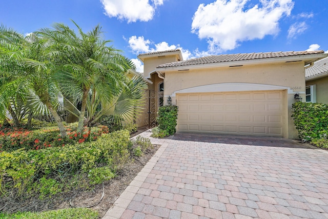 mediterranean / spanish-style house with stucco siding, a tiled roof, a garage, and decorative driveway