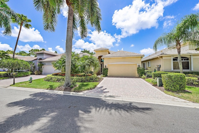 mediterranean / spanish-style house featuring stucco siding, a tiled roof, a garage, and decorative driveway