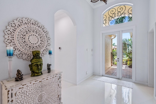 foyer entrance with arched walkways, baseboards, french doors, light tile patterned flooring, and a towering ceiling
