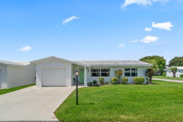 ranch-style house featuring a garage, driveway, a front yard, and stucco siding
