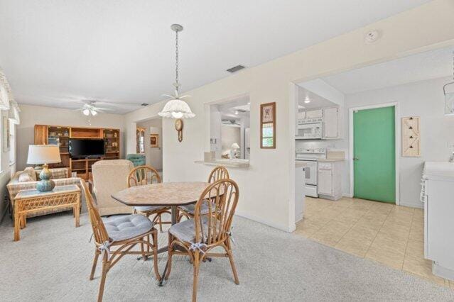 dining area featuring a ceiling fan, light carpet, light tile patterned floors, and baseboards