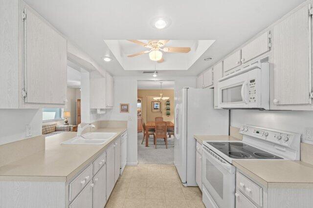 kitchen with white appliances, a tray ceiling, a ceiling fan, and light countertops