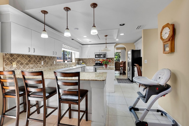 kitchen featuring appliances with stainless steel finishes, a peninsula, tasteful backsplash, arched walkways, and healthy amount of natural light