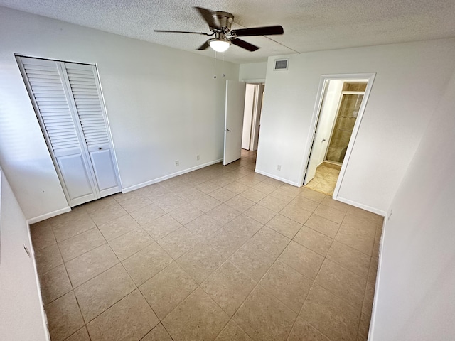 unfurnished bedroom featuring a textured ceiling, light tile patterned flooring, baseboards, a ceiling fan, and connected bathroom