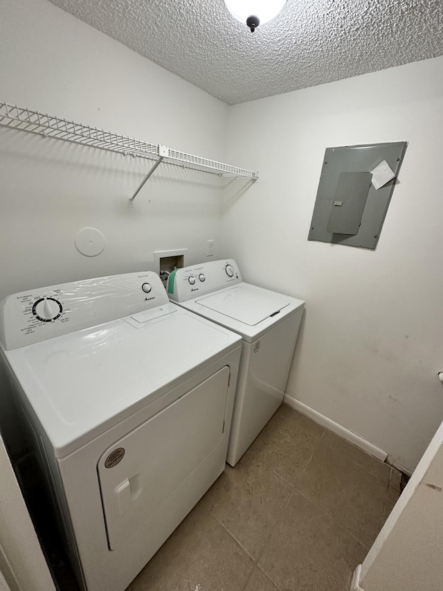 washroom with electric panel, washer and clothes dryer, baseboards, a textured ceiling, and light tile patterned flooring