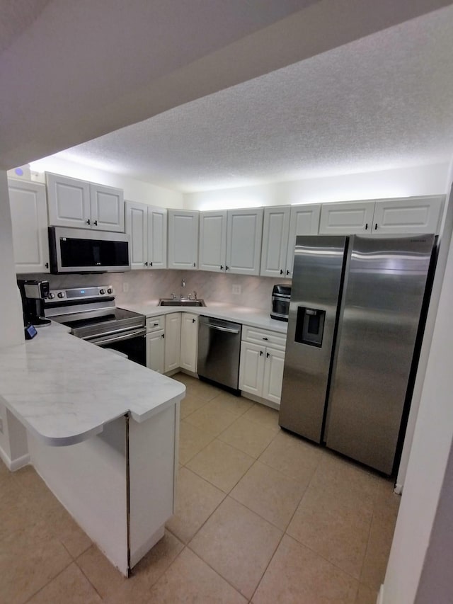 kitchen with stainless steel appliances, a peninsula, a sink, light tile patterned flooring, and a textured ceiling