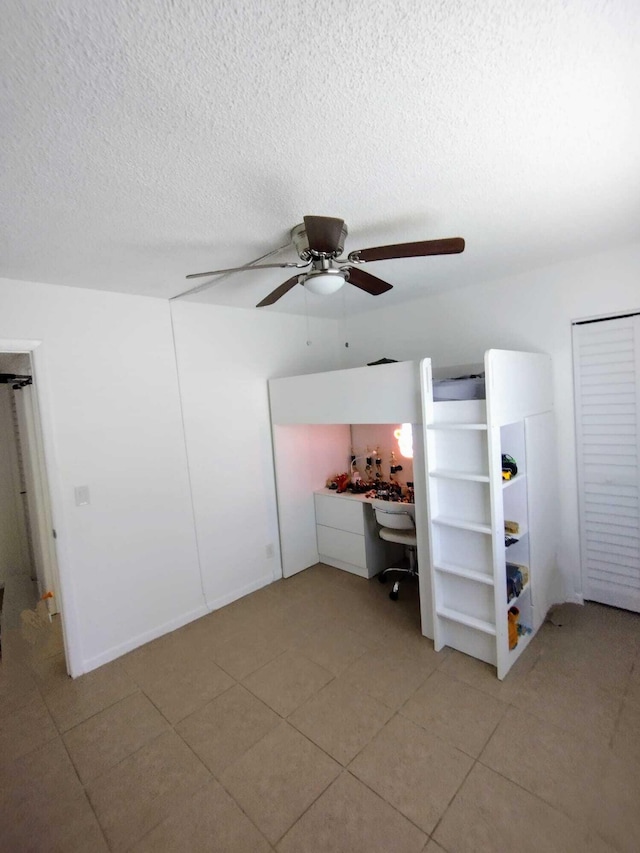 unfurnished bedroom with an office area, light tile patterned flooring, a textured ceiling, and a ceiling fan