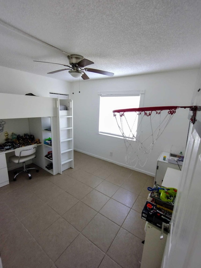 spare room with a desk, a textured ceiling, a ceiling fan, baseboards, and tile patterned floors