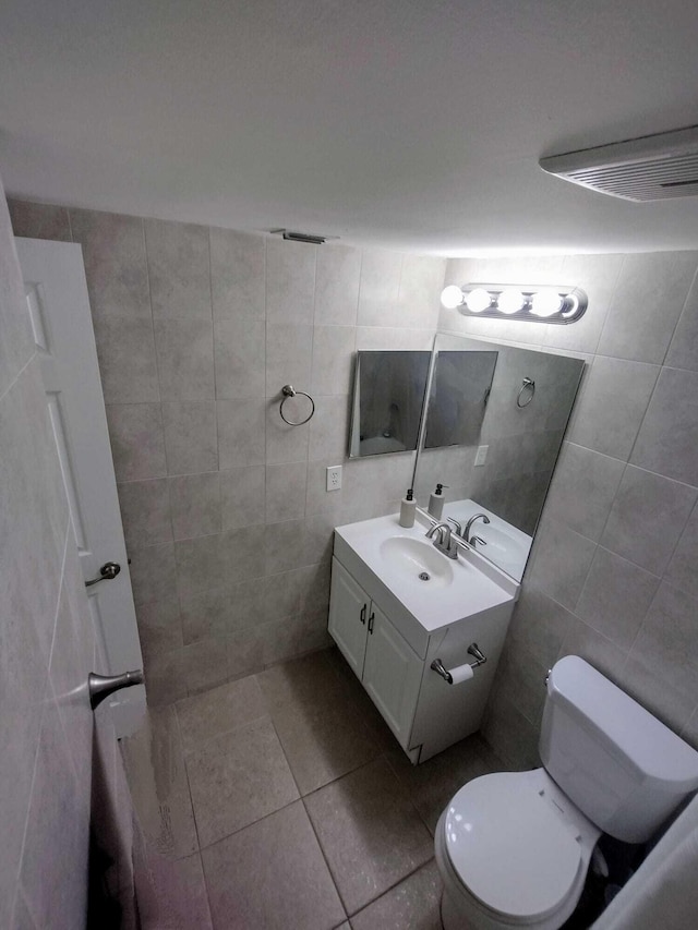 bathroom with tile walls, vanity, toilet, and tile patterned floors