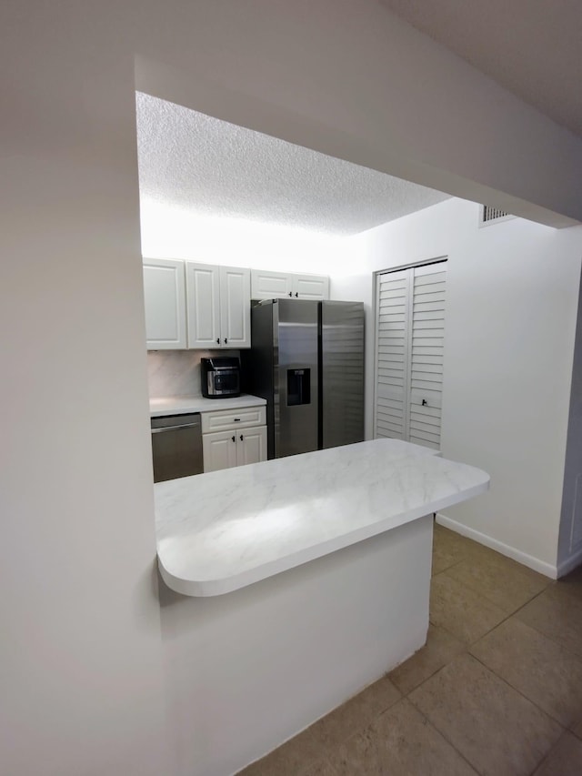 kitchen with appliances with stainless steel finishes, tile patterned flooring, white cabinets, a peninsula, and baseboards