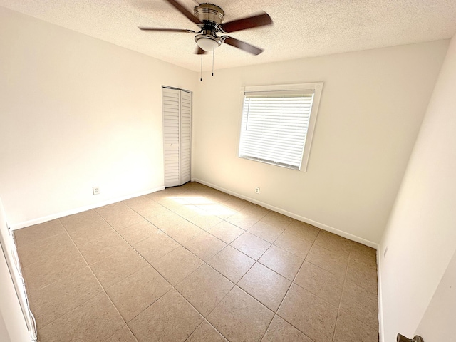 spare room featuring a textured ceiling, ceiling fan, tile patterned flooring, and baseboards