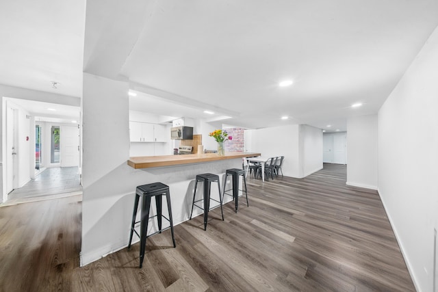 356 SE Prima Vista Blvd, Port Saint Lucie, FL 34983 - kitchen with stainless steel microwave, a breakfast bar area, wood finished floors, baseboards, and white cabinetry