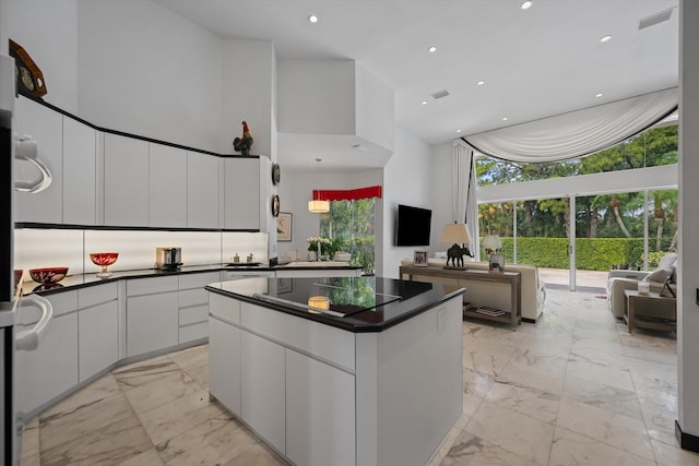 kitchen with a towering ceiling, light marble finish floors, dark countertops, a center island, and white cabinetry