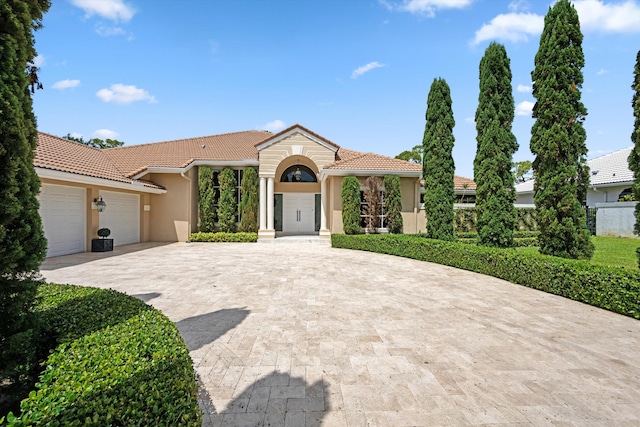 mediterranean / spanish home featuring a garage, a tile roof, decorative driveway, and stucco siding
