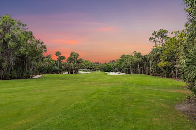 view of community with golf course view, a yard, and view of wooded area