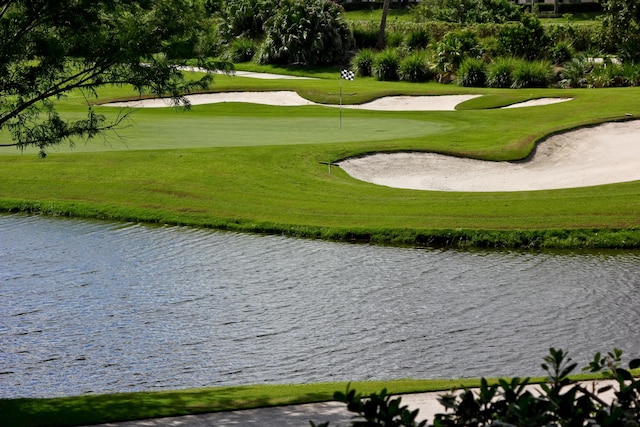 view of property's community with a water view, golf course view, a yard, and a putting area