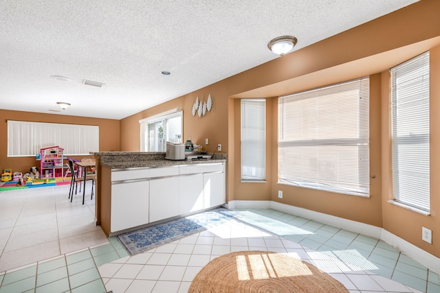 1915 Capeside Cir, Wellington, FL 33414 - kitchen featuring light tile patterned flooring, a peninsula, white cabinets, plenty of natural light, and a textured ceiling
