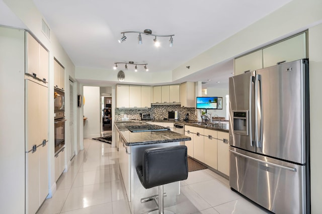 kitchen with black appliances, cream cabinets, tasteful backsplash, a center island, and light tile patterned floors