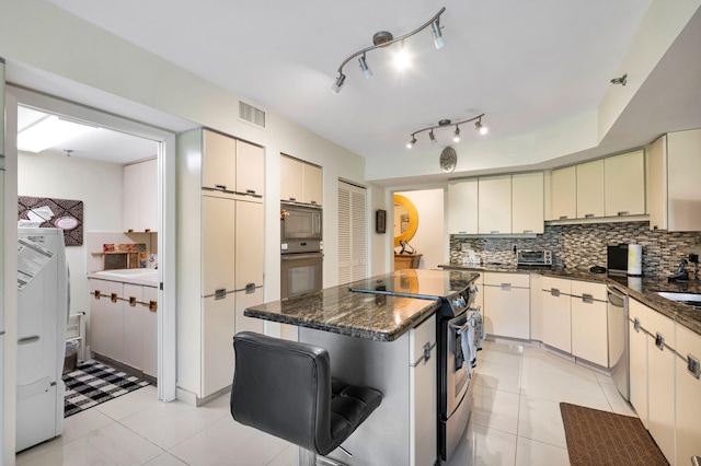 kitchen featuring stainless steel appliances, tasteful backsplash, cream cabinets, and dark stone countertops